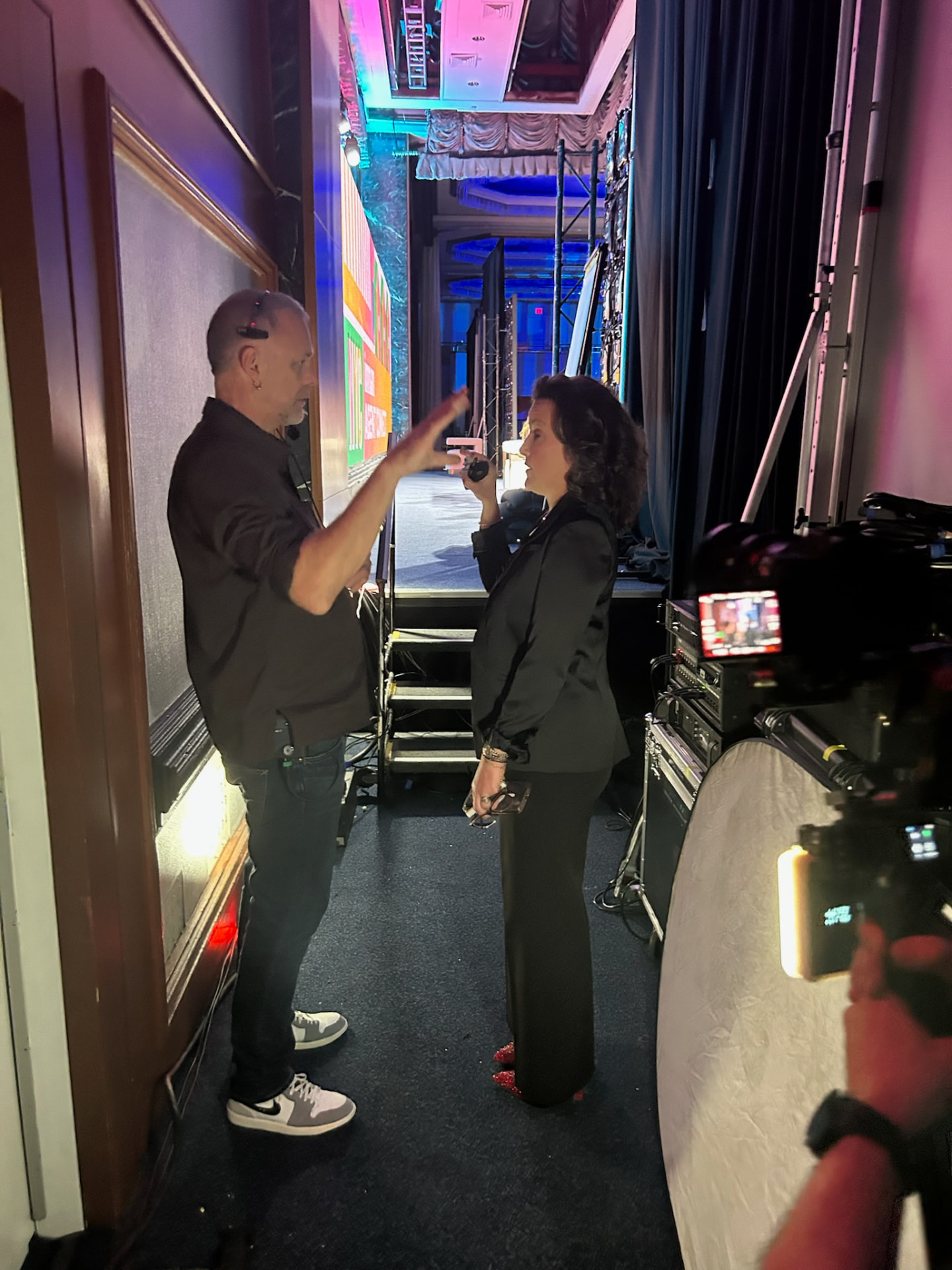 Renee Funk and a stage manager walk through cues backstage, with stage lights and monitors behind them