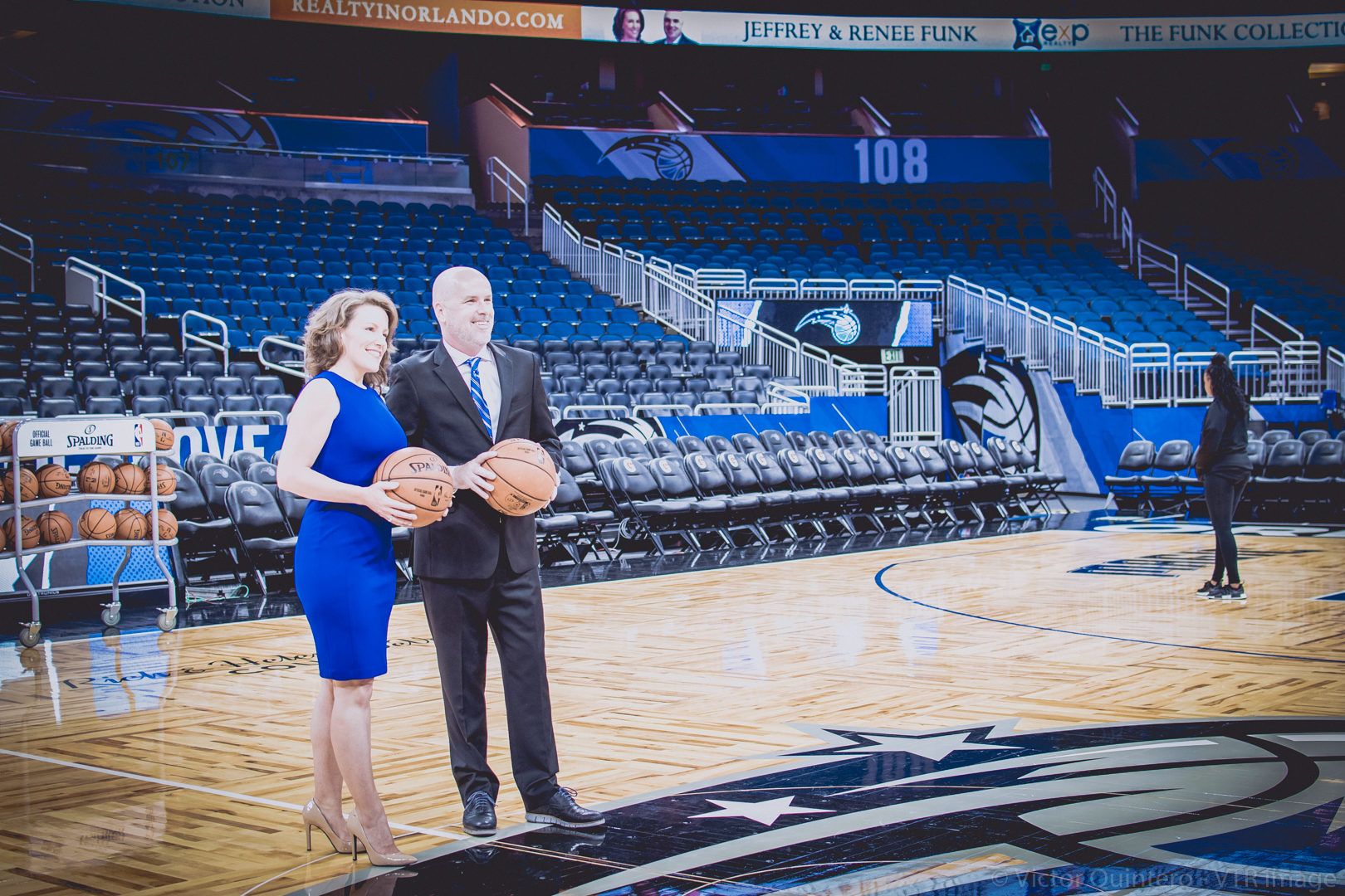 Jeff and Renee Funk on the Orlando Magic court at Amway Center, holding basketballs in front of their courtside signage.